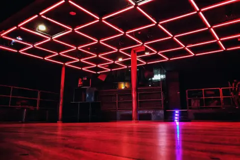 Interno di un basic club con luci al neon rosse sul soffitto e pavimento in legno.