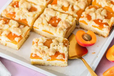 Saftiger aprikosenkuchen mit buttrigen streuseln, perfekt für den Sommer. Ein Stück ist mit einem goldenen Kuchenheber herausgenommen.