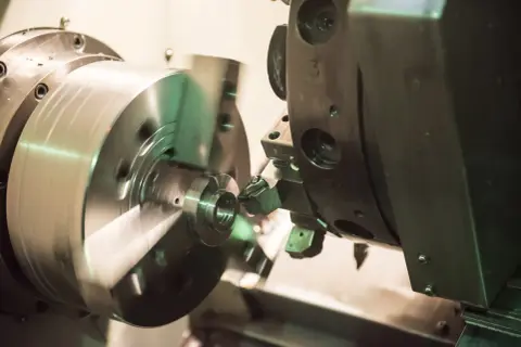 Precyzyjne toczenie aluminium na obrabiarce CNC. Metalowy element obraca się, a narzędzie precyzyjnie nadaje mu kształt.
