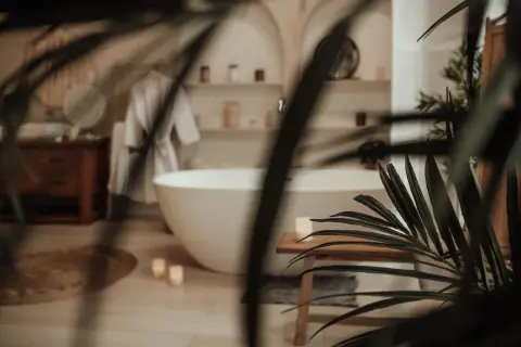 Une baignoire îlot blanche dans une **chaleureux salle de bain zen**. Un peignoir blanc est suspendu, des bougies allumées et des plantes apportent une touche de sérénité.