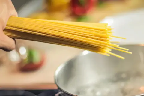 Dłoń trzymająca pęczek spaghetti nad gotującą się wodą. Zastanawiasz się, jaki makaron ma najmniej kalorii?