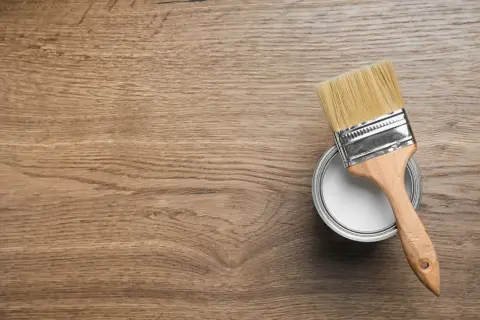 Pennello e barattolo di vernice bianca su fondo in legno, pronti per iniziare a come verniciare un mobile in legno.