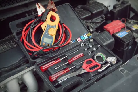 Verktygslåda med startkablar, tångamperemeter och andra verktyg redo för att kontrollera plus och minus batteri i bilen.
