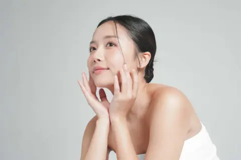 Mujer asiática con piel radiante, acariciando su rostro. Su secreto: agua de arroz para la cara.