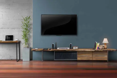 Moderner fernseher im wohnzimmer, daneben ein schlichtes Sideboard mit Deko und Büchern.