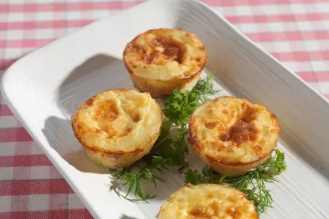 Små, gyllene potatis i muffinsform, serverade med färska örter på en vit bricka. Perfekt som tillbehör eller plockmat.