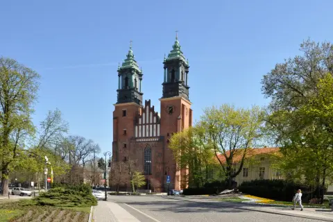 Imponująca katedra w Poznaniu z dwiema wieżami i zielonymi dachami, otoczona drzewami i budynkami.