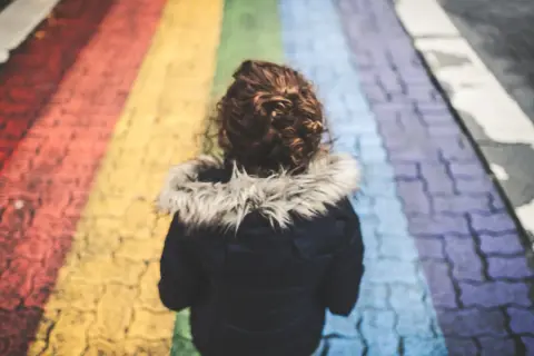 Dziecko z kręconymi włosami idzie po tęczowym przejściu dla pieszych.