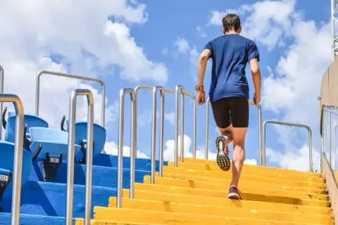 Un homme en tenue de sport monte des escaliers jaunes, un entraînement de renfo course à pied sous un ciel bleu.