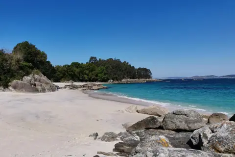 Arena blanca, aguas turquesas y rocas salpican la **playa de Castiñeiras**, un rincón idílico bajo un cielo azul intenso.
