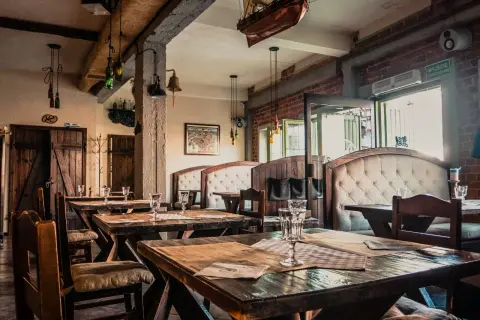 Wnętrze restauracji z drewnianymi stołami i wygodnymi kanapami. Na ścianie wisi model statku, nawiązujący do morskiego klimatu, jak w gdańskim bowke.