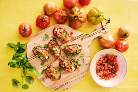Bruschetta recept med färska tomater och basilika på en träskärbräda, omgivet av mogna tomater.