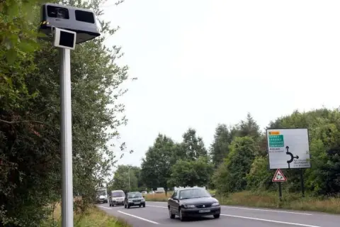 Un radar leurre sur un poteau, avec des voitures sur la route et un panneau de signalisation.