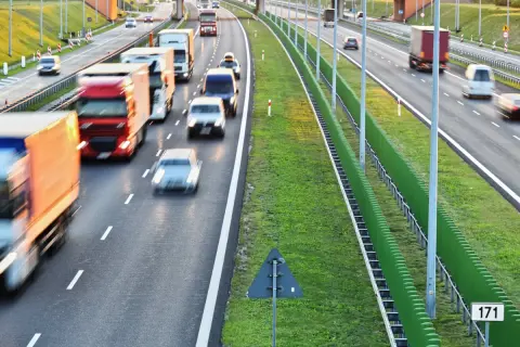 Autostrada z ruchem samochodowym i ciężarowym, zielone ekrany akustyczne i znak drogowy.