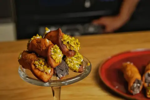 Ein Glasständer voller Cannoli, garniert mit Pistazien und Schokolade. Ein köstliches Cannoli-Rezept zum Nachmachen.