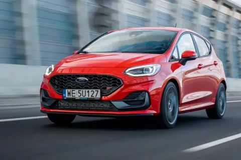 Czerwony Ford Fiesta ST pędzi po drodze, błyszcząc w słońcu.