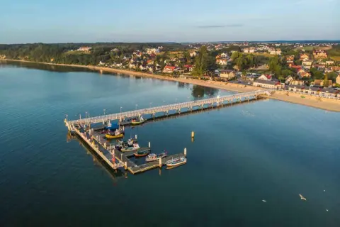Molo w Mechelinkach z łodziami i widokiem na plażę i zabudowania. To świetne mechelinki atrakcje dla każdego.