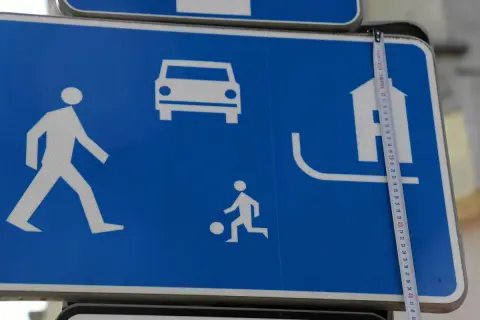 Znak D18: strefa zamieszkania z pieszym, dzieckiem bawiącym się piłką, samochodem i domem.
