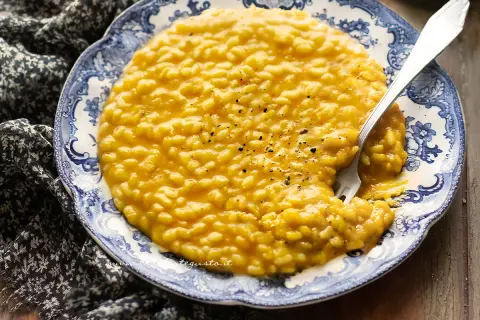 Un cremoso risotto alla zucca, servito su un piatto decorato, con una forchetta che affonda nel piatto.