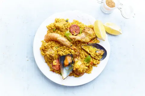 Une assiette de paella royale, garnie de crevettes, moules, poulet, chorizo et riz jaune, avec des quartiers de citron.