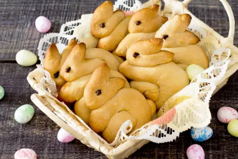Korb voller goldbrauner Quark Osterhasen, umgeben von bunten Ostereiern auf dunklem Holz.