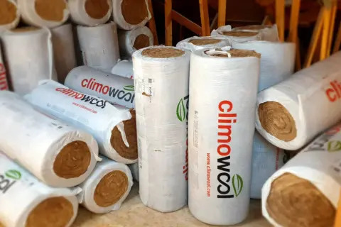 Zwoje wełny mineralnej, gotowe do utylizacji lub ponownego wykorzystania. Materiał izolacyjny w opakowaniach z logo "climowool".