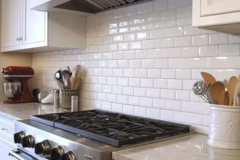 A clean kitchen backsplash installation with white subway tiles, a red stand mixer, and cooking utensils.
