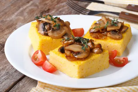 Trzy kwadratowe porcje polenty, podane z duszonymi pieczarkami i pomidorkami koktajlowymi. Pyszne danie, które pokazuje, co to polenta.