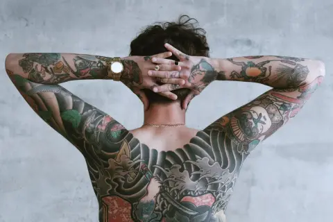 Mężczyzna z rękami za głową, prezentujący rozbudowane tatuaże w stylu irezumi polska.