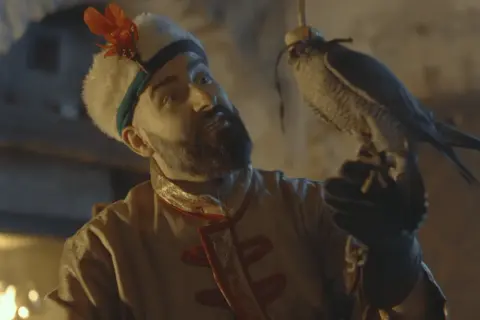 Mężczyzna w stroju z epoki, z sokolniczą rękawicą, trzyma ptaka. Może to być scena z teledysku "Hej Sokoły".