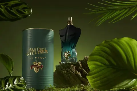 Flakon perfum Jean Paul Gaultier Le Beau Le Parfum w otoczeniu zielonych liści i mchu.
