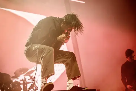 Chino Moreno z Deftones na koncercie w Polsce, w ogniu czerwonych świateł, śpiewa z pasją.