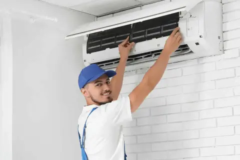 Tecnico con cappellino blu esegue la sanificazione aria condizionata, controllando i filtri per un'aria più pulita.