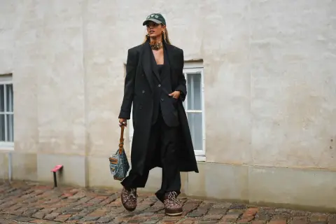 Elegancka stylizacja z czapką z daszkiem. Kobieta w czarnym garniturze i płaszczu, z torebką i modną czapką.