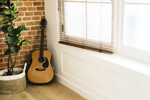 Akustyczna gitara, idealna na sto lat na gitarze dla początkujących, stoi przy ceglanej ścianie obok rośliny w koszu.