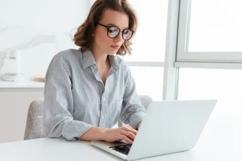 Kobieta w okularach pracuje na laptopie, szukając informacji o **santander zamknięcie konta**.