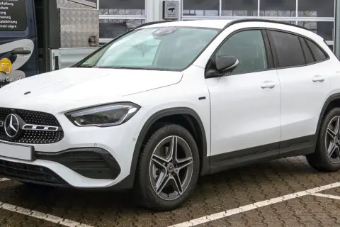 Biały Mercedes GLA, kompaktowy SUV, zaparkowany na mokrym parkingu. Jego wymiary idealnie pasują do miejskiej dżungli.