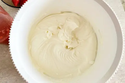 Gładka, kremowa masa z mascarpone w białej misie, gotowa do deseru. Obok widać miseczkę z truskawkami.