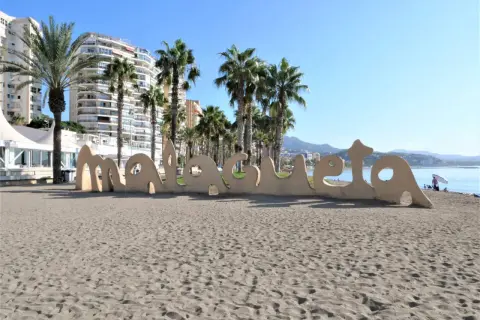 Malaga plaże: piasek, palmy i napis "Malaga" na tle budynków i morza.