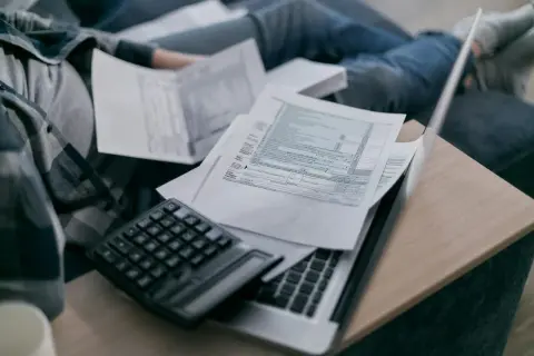 Osoba przegląda dokumenty, w tym rachunek za prąd, z kalkulatorem i laptopem.