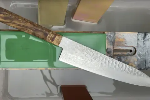 Ein japanisches Messer mit Damastmuster wird auf einem Schleifstein mit präzisem Schleifwinkel geschärft.
