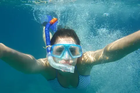 Dziewczyna w masce i rurce do oddychania pływa pod wodą. To właśnie snorkeling – odkrywanie podwodnego świata!