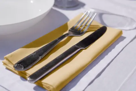 Un couteau et une fourchette reposent sur un noeud serviette de table jaune, prêt pour un repas.
