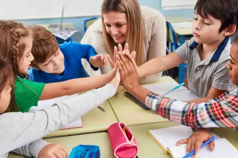 Niños y maestra celebran con un choque de manos, fomentando la motivación en el aula.