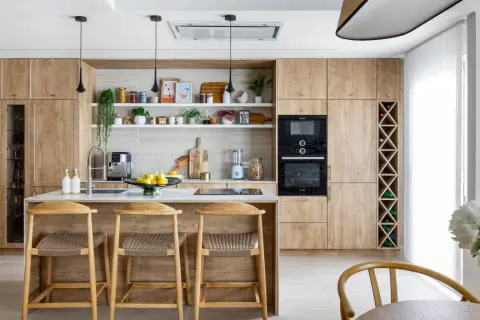 Cocina moderna con armarios de madera clara, isla central con taburetes y estanterías decoradas. Ideal para inspiración de decoracion cocinas.