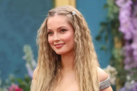 Hannah Dodd, con cabello rubio ondulado y adornos florales, sonríe con un vestido plateado.