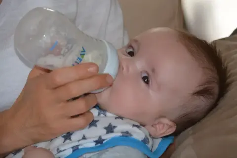 Rączka podaje butelkę z mlekiem 5-miesięcznemu dziecku, które pije z zapałem.