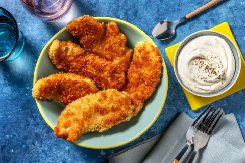 En tallrik med gyllene, krispig kyckling som ser utsökt ut. Bredvid finns en skål med krämig dipp och bestick.
