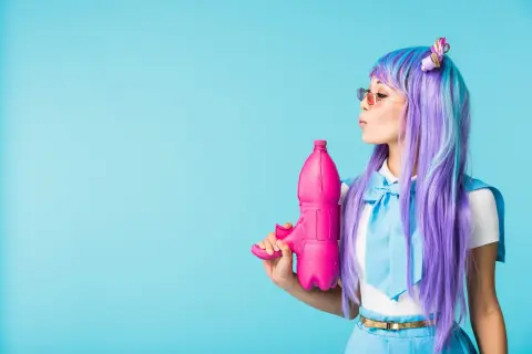 Dziewczyna w peruce w stylu kawaii z fioletowymi i niebieskimi włosami trzyma różowy pistolet na wodę.