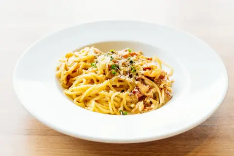 Spaghetti carbonara authentique dans une assiette blanche, garnie de lardons et de parmesan.